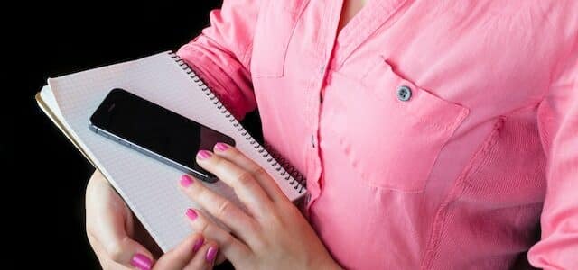 Woman in pink button down shirt holding phone and notebook